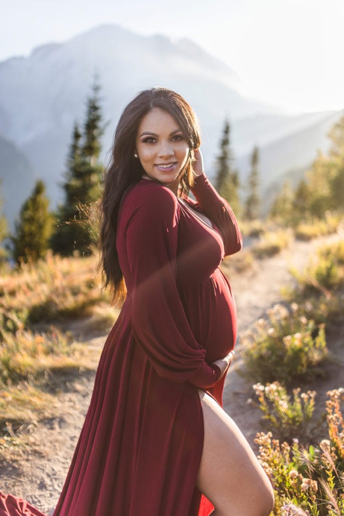 Maternity Photographer, an expecting mother holds her pregnant belly on a wooded trail in the mountains
