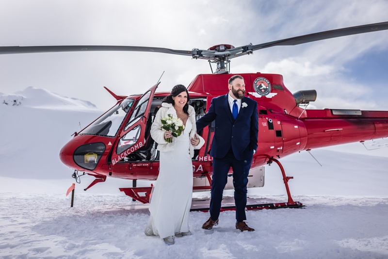 Adventure Elopement Photographer, Bride and Groom stand in the snow before a helicopter