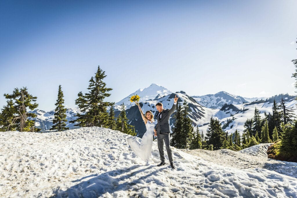 Couple in wedding attire on top of Mount Baker posing for a photo in the snow with mountain backdrop