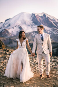 Newly married couple holding hands and walking with Mt. Rainier snow capped mountain in background